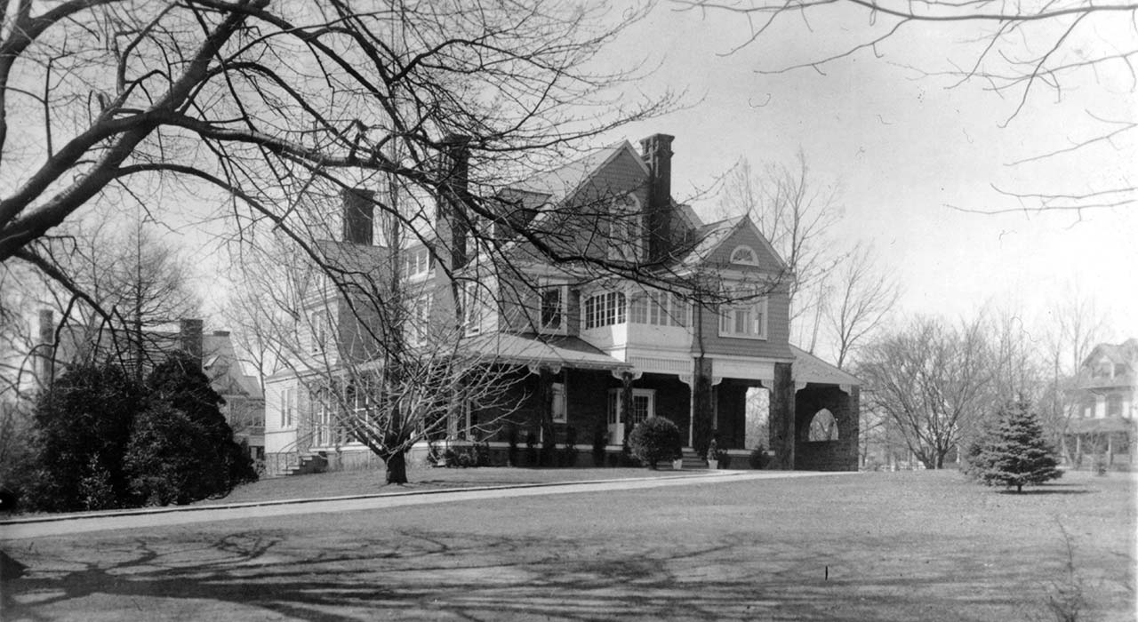 large mansion on open lawn with bare trees; other large homes on left and right in background