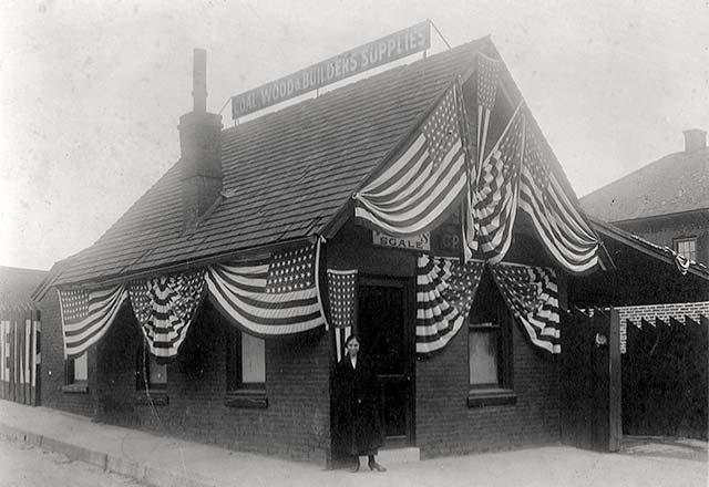 one-story dark brick building draped in flags; a woman stands in the doorway.