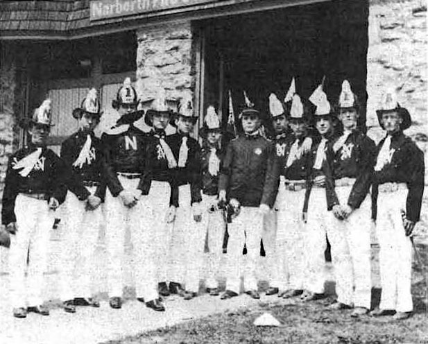 Twelve firemen in dress uniform posed in front of the Narberth fire station