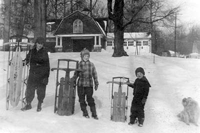 three children holding sleds and a dog on a snowy slope