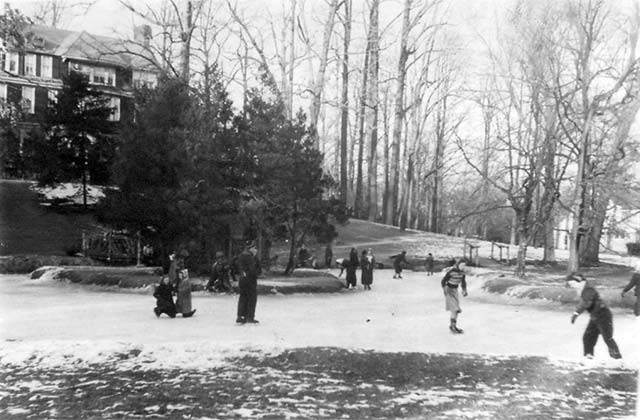 children skating on pond with house up hill in background