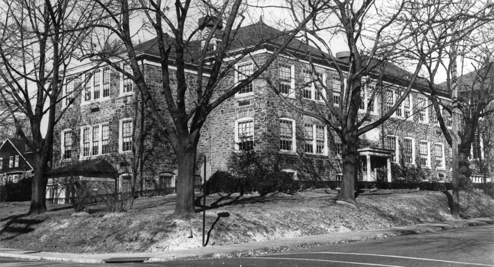 dark stone 3-story building, large trees in front