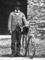 A Black man holding a bicycle in front of a stone building
