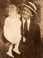 older man with straw hat looks lovingly at a toddler he's holding in his arms