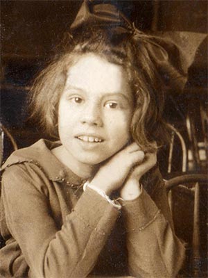 young girl with huge hair bow posed with face leaning on clasped hands