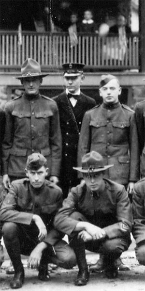 men in military unifonms posed in two rows in front of a porch with a family on it