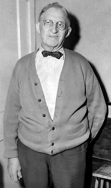 smiling older man wearing glasses, v-neck sweater and bow tie