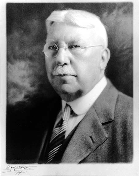 head and shoulders formal photo portrait of a white haired man with nustache, metal frame glasses, old fashioned collar