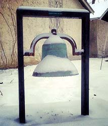 snow-covered bell hangs in a metal frame