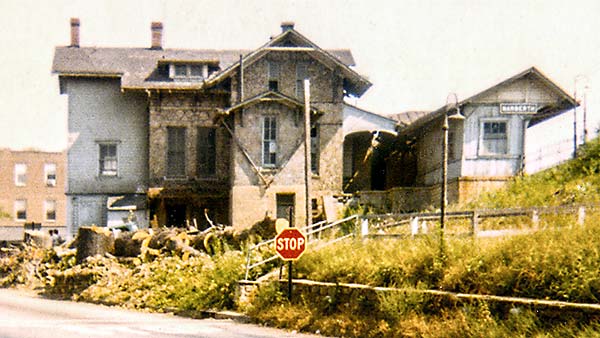 3-story stone building with wood extension built on hillside next to train station shelter