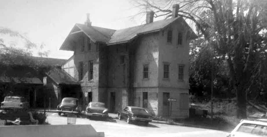 Three-story stone and wood building surrounded by parking with cars from the 1950s and 60s.