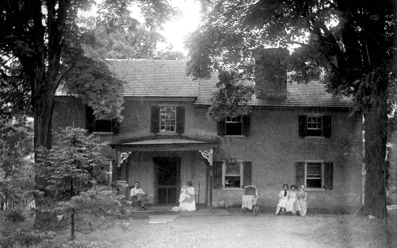 Husband, wife holding a child and three children seated in front of the house