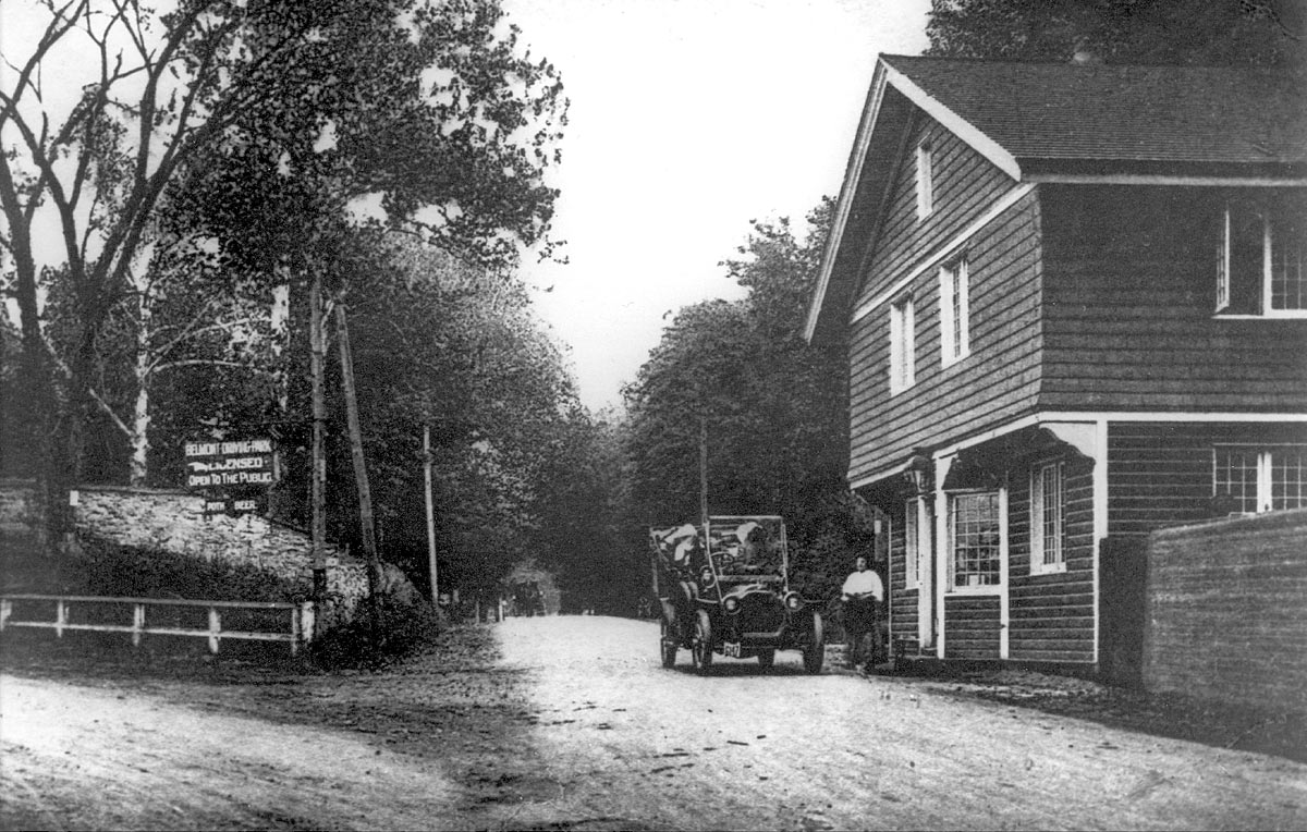 A vintage car sits in front of the toll house. The toll keeper stands in front.