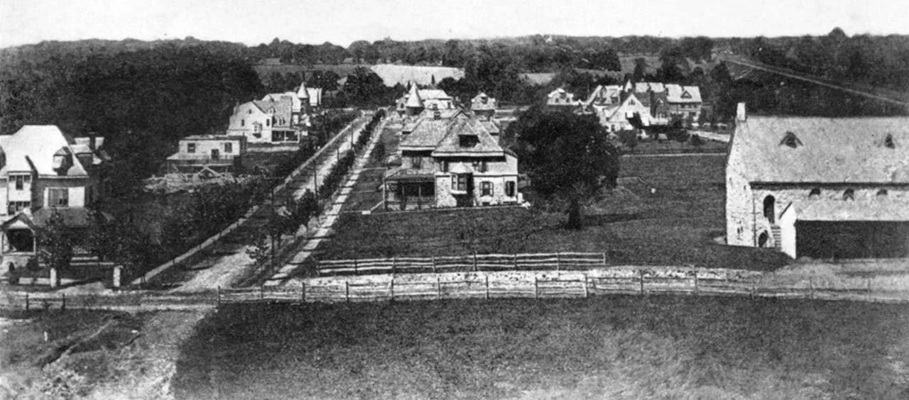 A roof-level view over south Narberth showing a dirt crossroads in the foreground, a dozen or so late Victorian houses, one under construction, and a stone church with a wood shed.