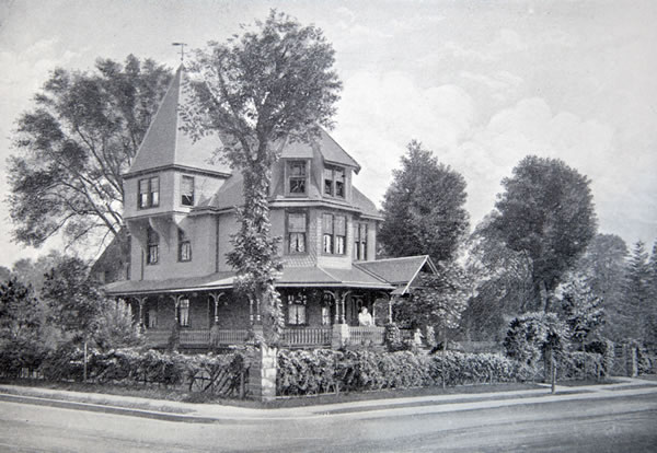 A lithograph of a three-story house with a square turret and wraparound porch, surrounded by a fence covered with plantings. A woman looks out from the porch, and a small child gestures from the front steps.